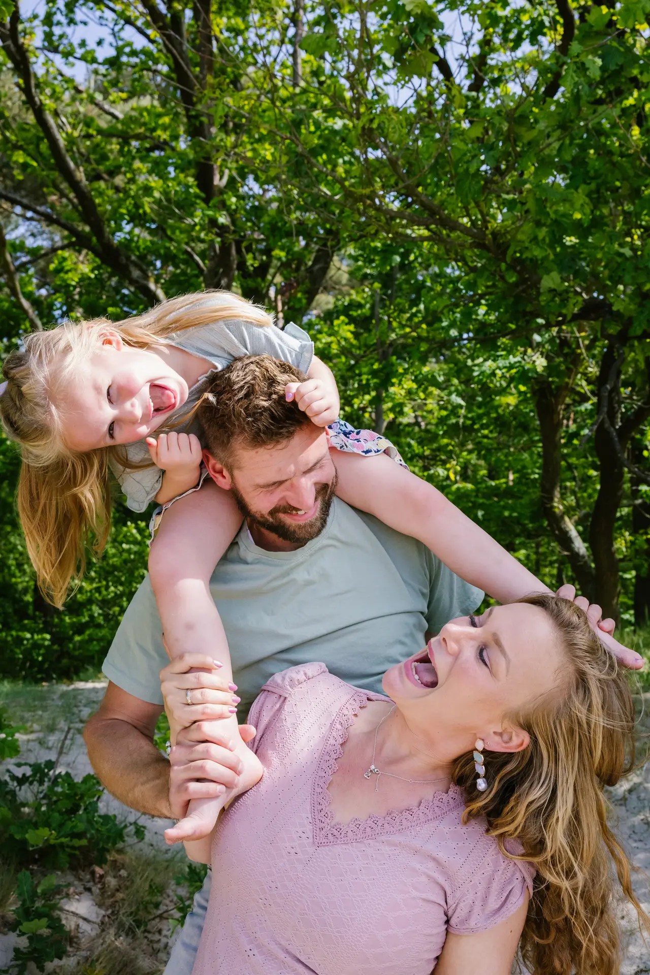 Gezin speelt en lacht samen tijdens een familieshoot in de natuur.