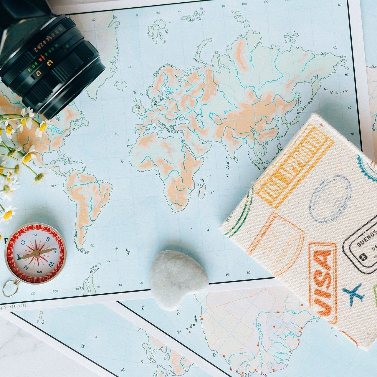 World map with a compass, camera and passport visa page laid out for trip planning