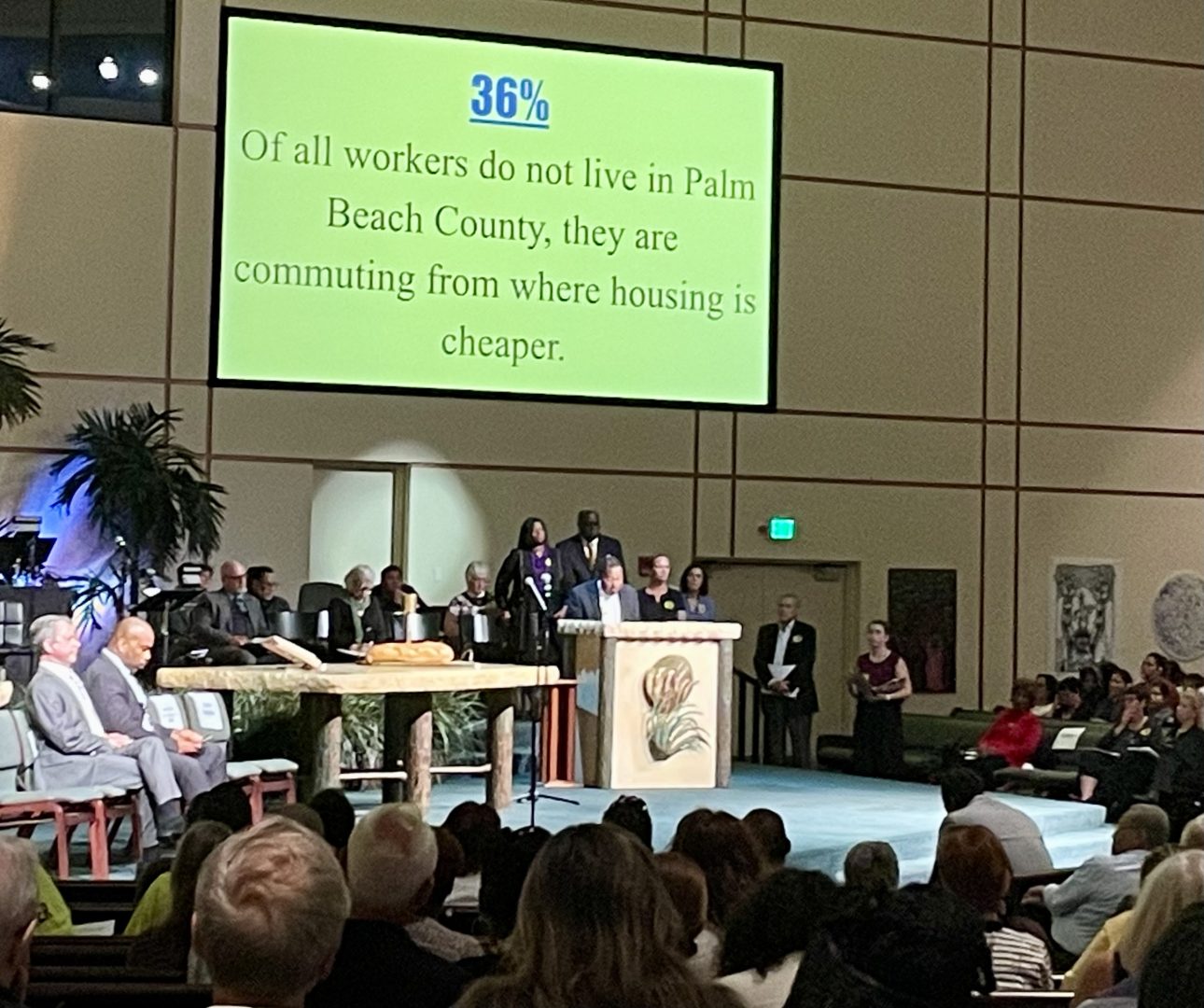 Commissioners seated under a large screen that shows a display to the crowd in a church sanctuary.