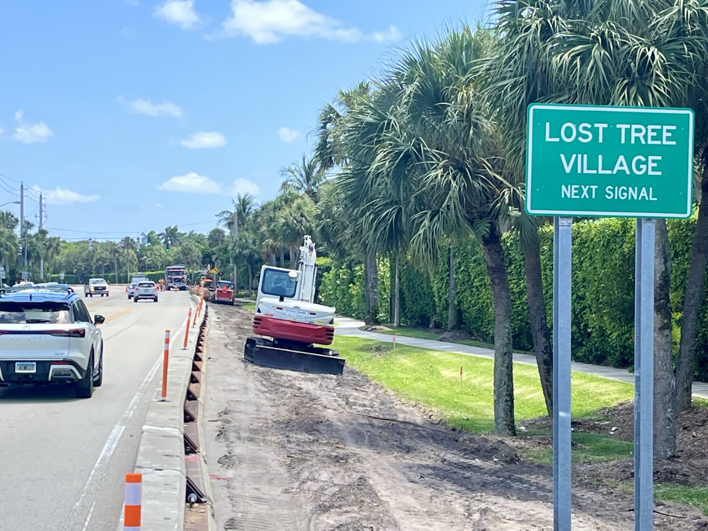 Construction equipment on side of the roadway with sign that says Lost Tree Village.