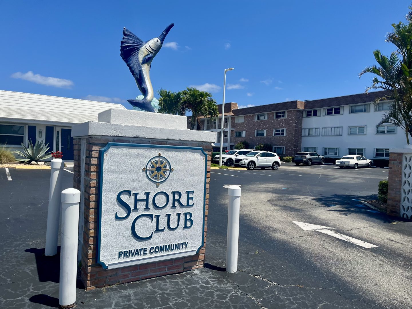 Sign that says Shore Club with three-story buildings in the background.