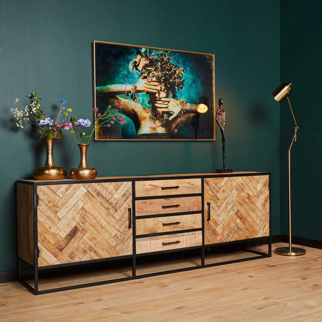 Een moderne kamer met de Dressoir Arlington 210 cm, gouden vazen met bloemen, een abstract menselijk beeld, een gouden staande lamp en een ingelijst kunstwerk van een persoon met handen die hun gezicht bedekken tegen een donkergroene muur.