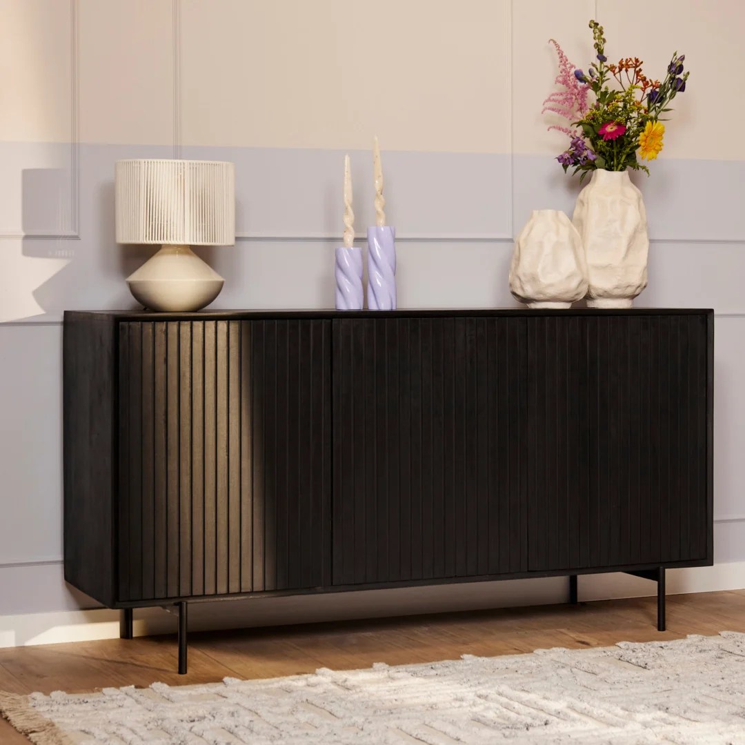 De REALITY Tafellamp BIDAR heeft een ovale vorm, metalen afwerking en geometrische uitgesneden patronen. Hij staat op een kleine houten voet en straalt een warm gouden licht uit voor een decoratieve touch.
