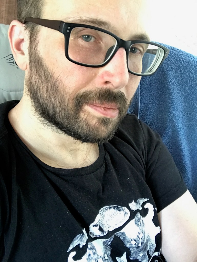 Middle aged white man with beard and dark framed glasses wearing a Death Kitty Shirt