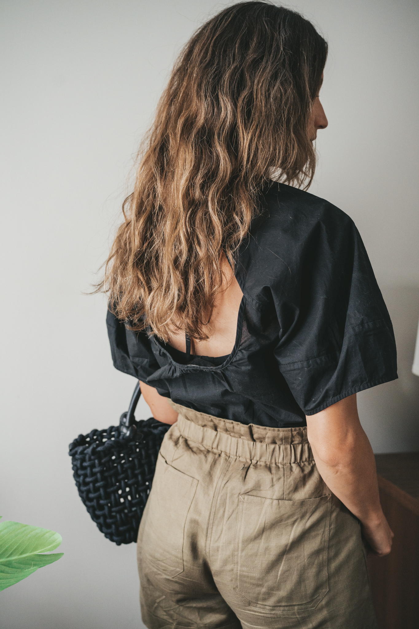 ashley wearing a black blouse, olive green paperbag shorts, black strappy sandals, a gold pendant necklace, and a black woven bag