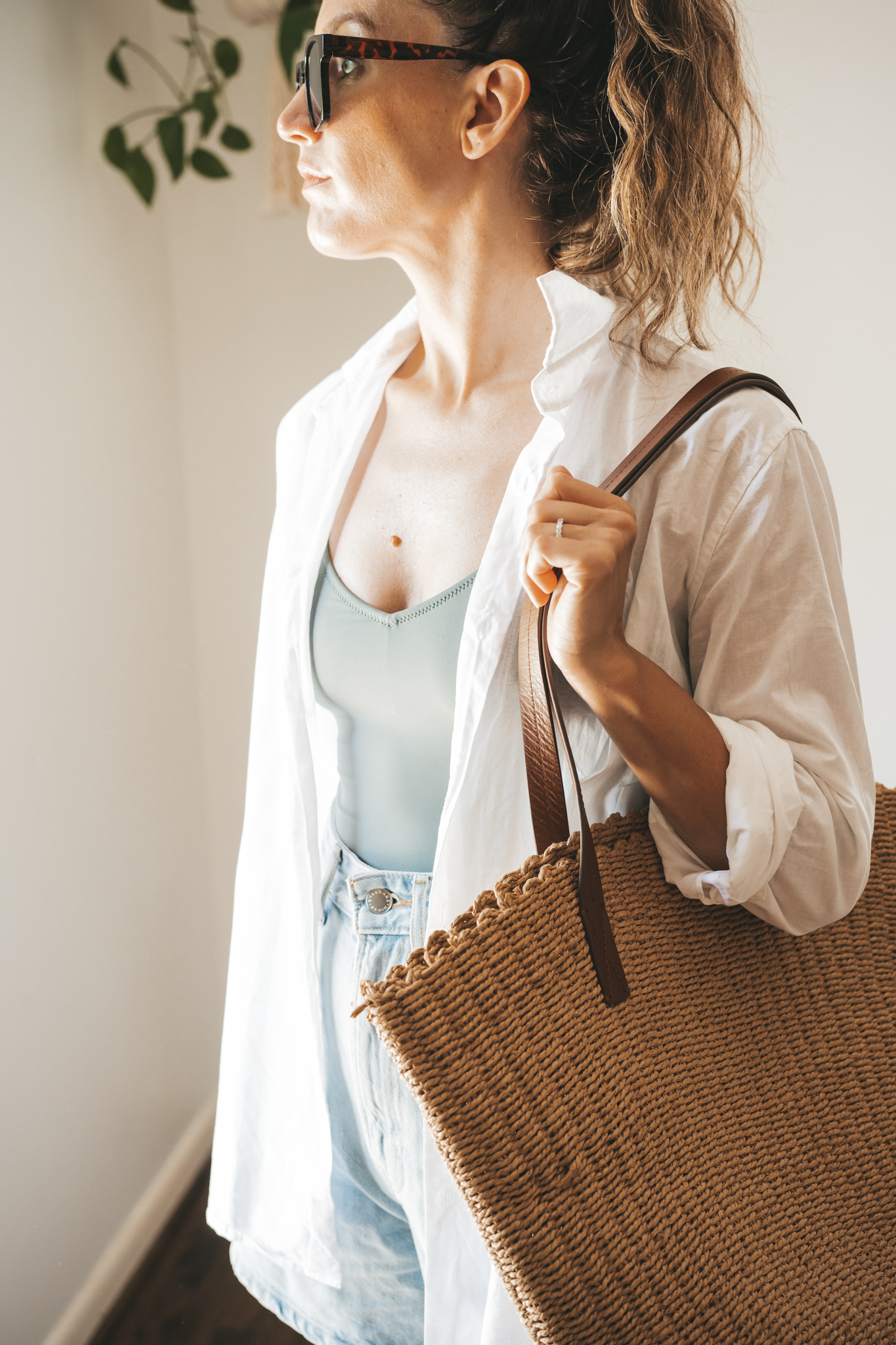ashley wearing an olive green one piece swimsuit under a white button down, light wash denim shorts, and white sandals with tortoise shell sunglasses