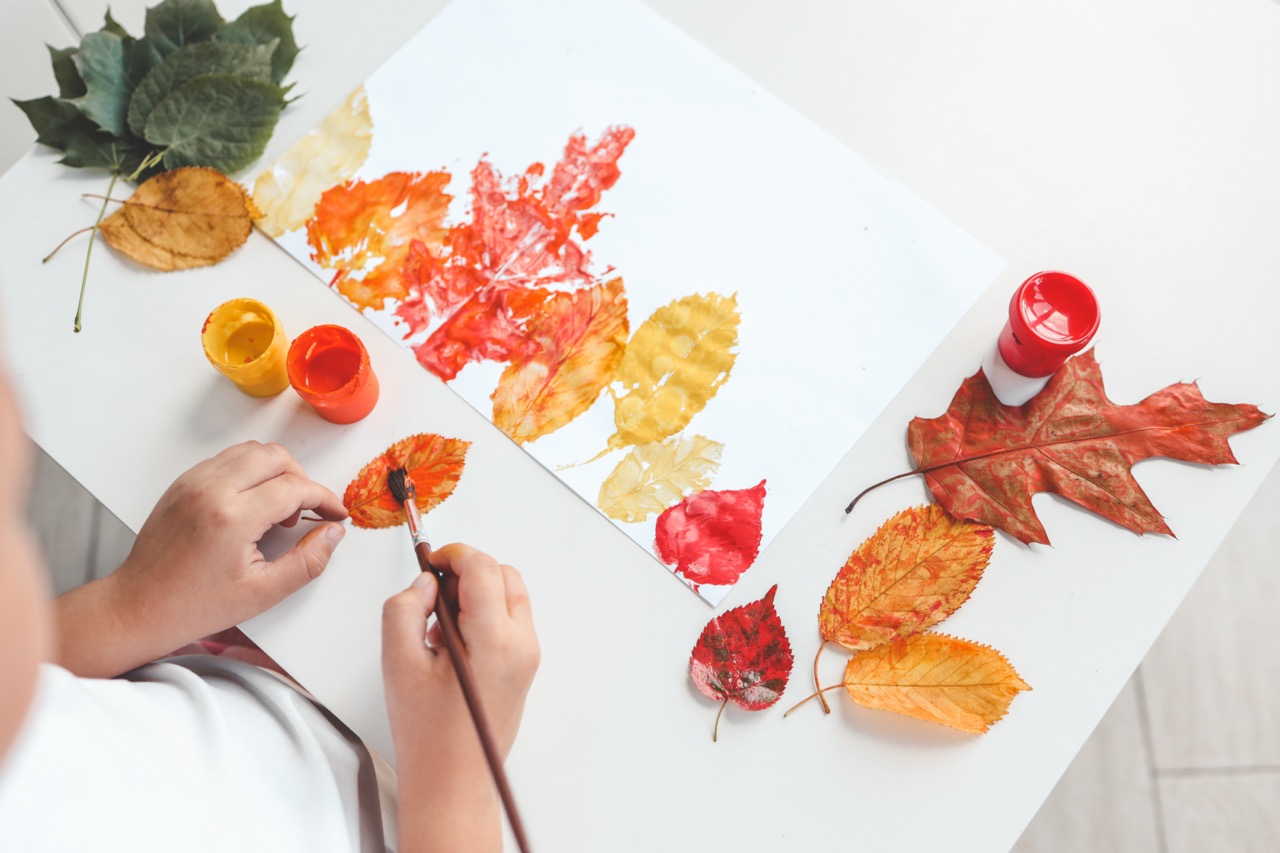 Little girl painting on autumn yellow leaves with gouache, kids arts, children creativity, autumn art.