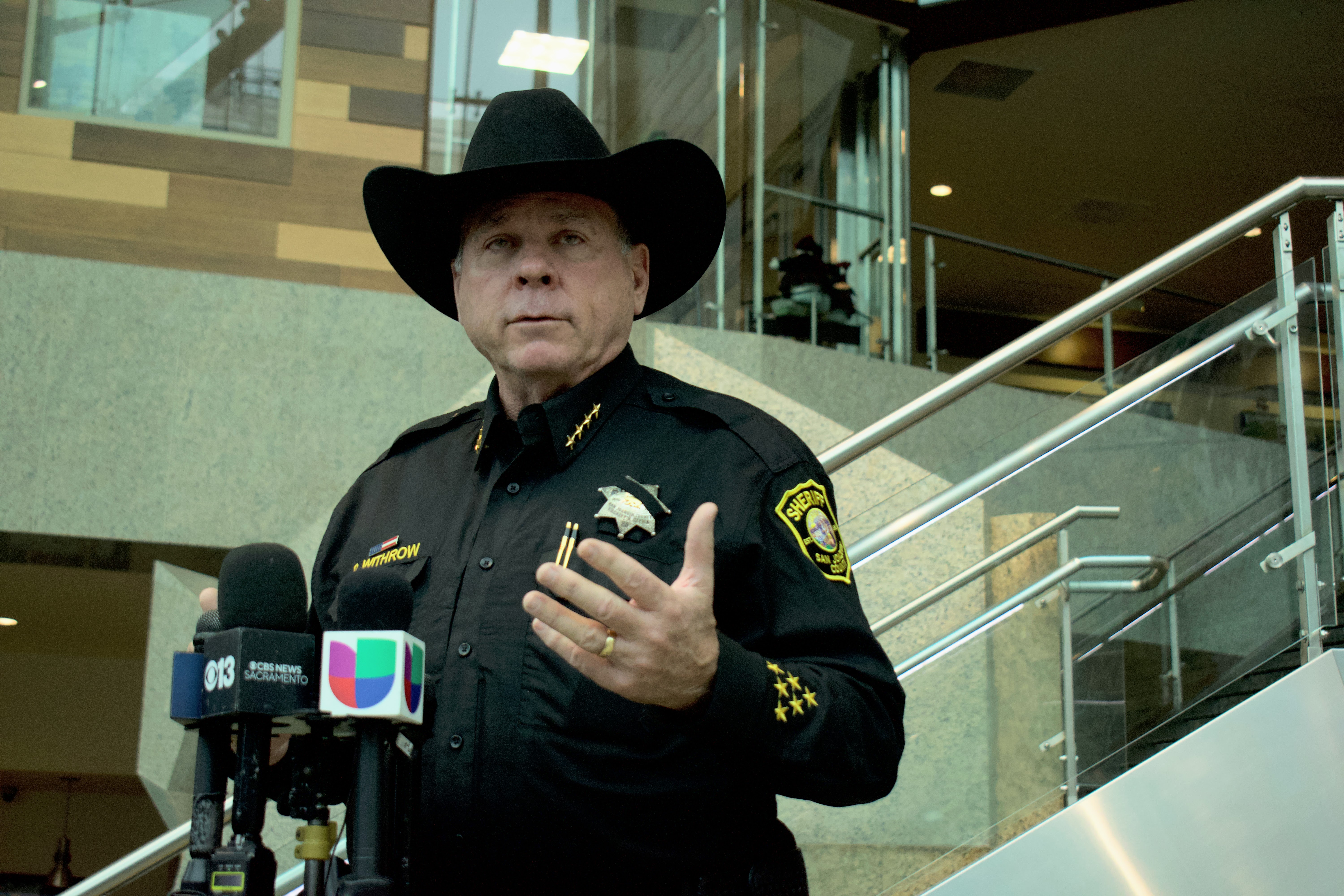 A person in a cowboy hat standing in front of a staircase and speaking into microphones