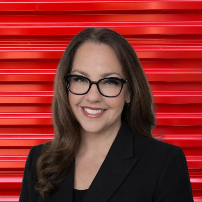 Colleen Barraclough, Vice President of Client Success at Storage Defender, standing in front of a red storage unit door