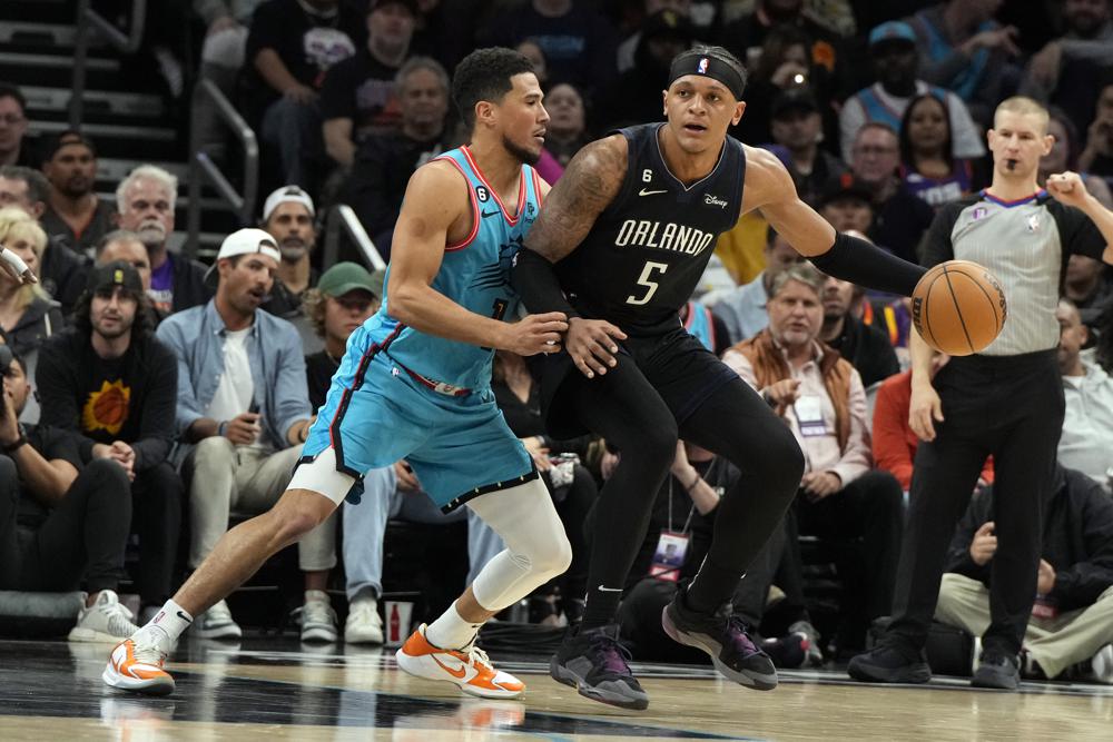 Phoenix Suns guard Devin Booker pressures Orlando Magic forward Paolo Banchero (5) during the second half of an NBA basketball game Thursday, March 16, 2023, in Phoenix. (AP Photo/Rick Scuteri)