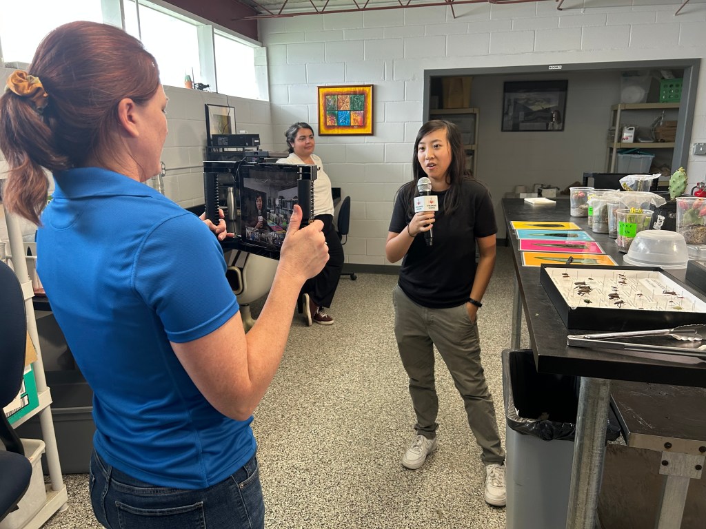 A graduate student uses an iPad to livestream an electronic field trip about insect weaponry in a lab.