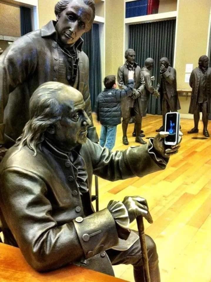StudioEIS’s seated bronze Benjamin Franklin in Signers’ Hall, Philadelphia, appears to hold up a smartphone as another bronze delegate stands behind him, with m…