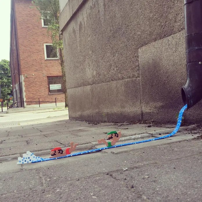 Pixelated Mario and Luigi swim along a blue bead-art stream running from a real drainpipe onto the sidewalk, by Pappas Pärlor.