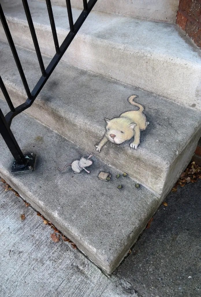 David Zinn chalk drawing of a pale cat reaching one paw down from a concrete step toward a tiny mouse beside a few crumbs on the step below, next to an iron rai…