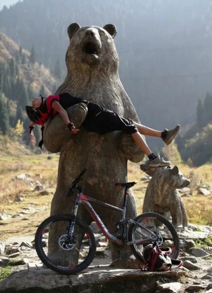 A mountain biker lies across the outstretched front legs of the big bear in the Three Bears sculpture at Ayusai Gorge in Almaty, Kazakhstan, with a bike at its…