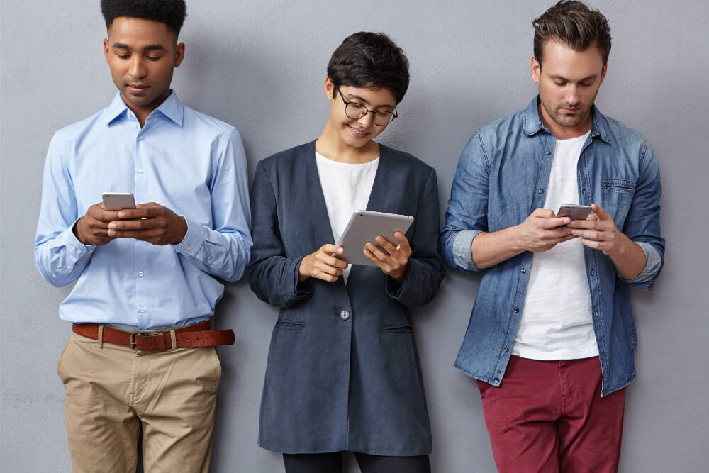 Three people standing together while actively using mobile devices