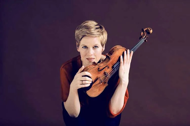 Violinist Isabelle Faust holding her instrument against a purple background