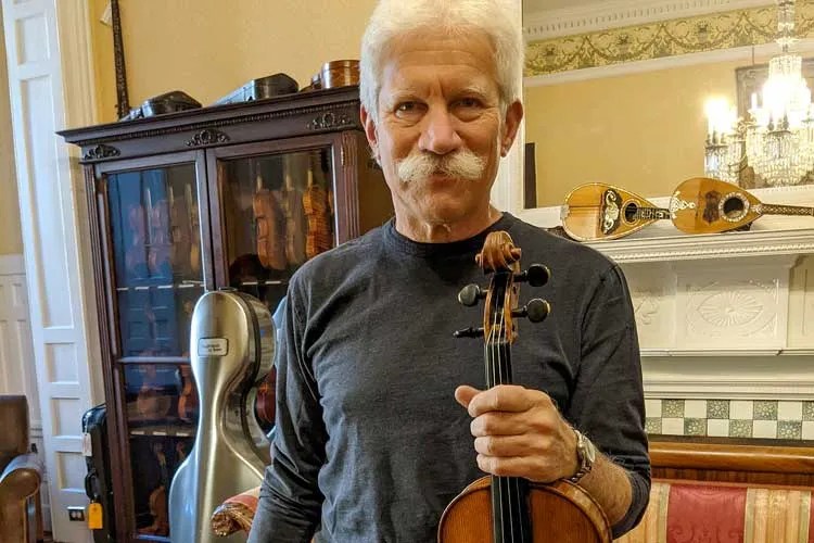 Adult violin player Fred Oster holds up a violin
