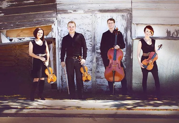 Apollo Chamber Players stand against a wall with their instruments