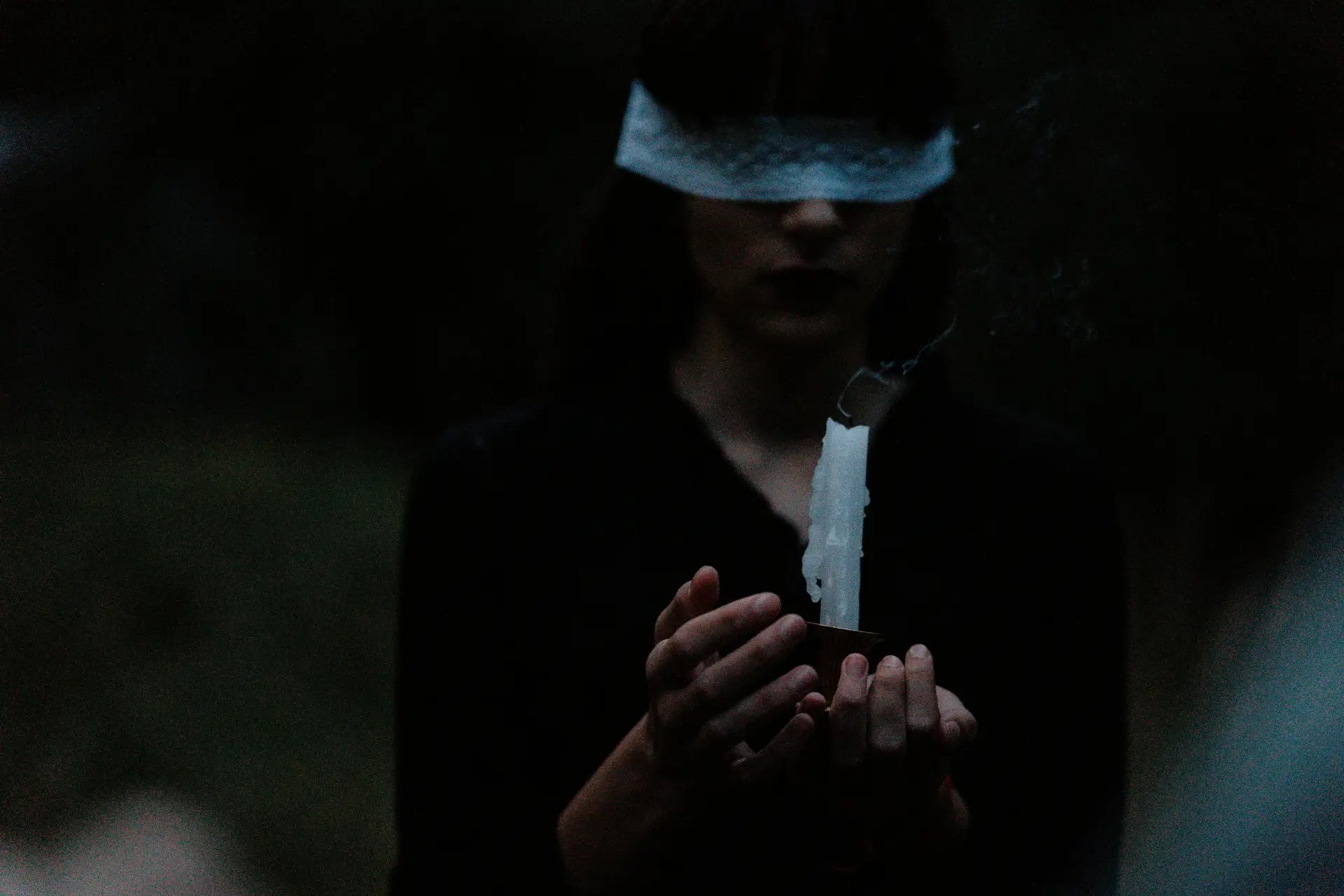 Blindfolded woman holding a candle.