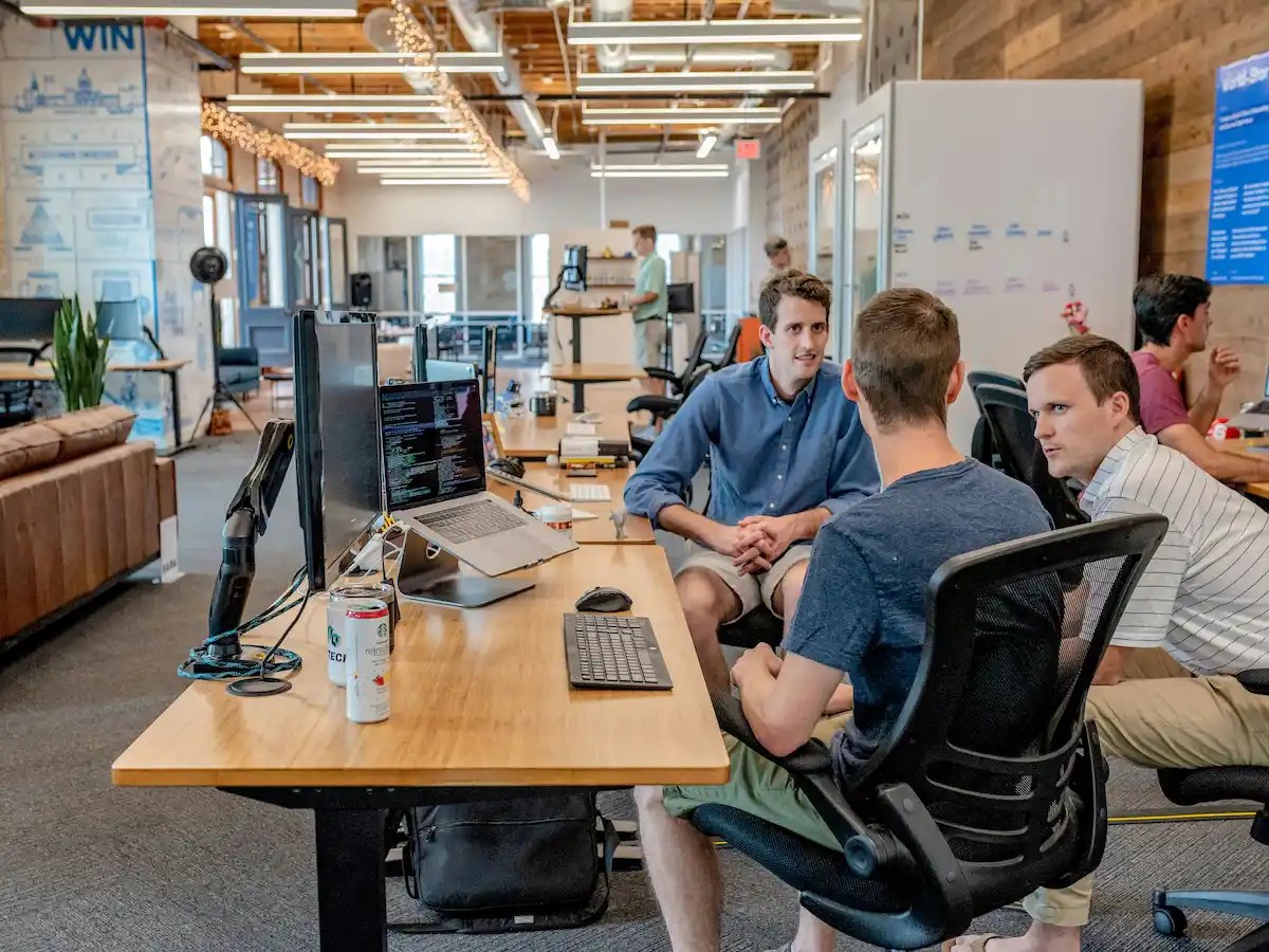 Employees collaborating inside a modern open-office workspace with computers, desks, and team discussions in progress.