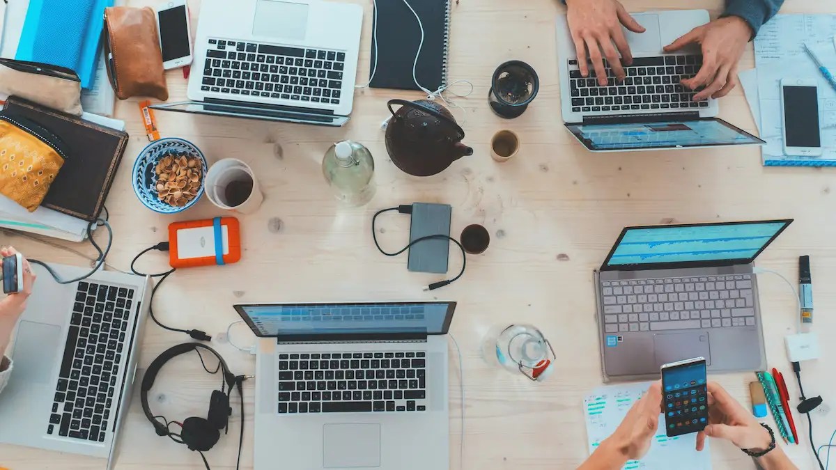 Overhead view of multiple people working on laptops, phones and notebooks around a shared table in a collaborative GCC workspace