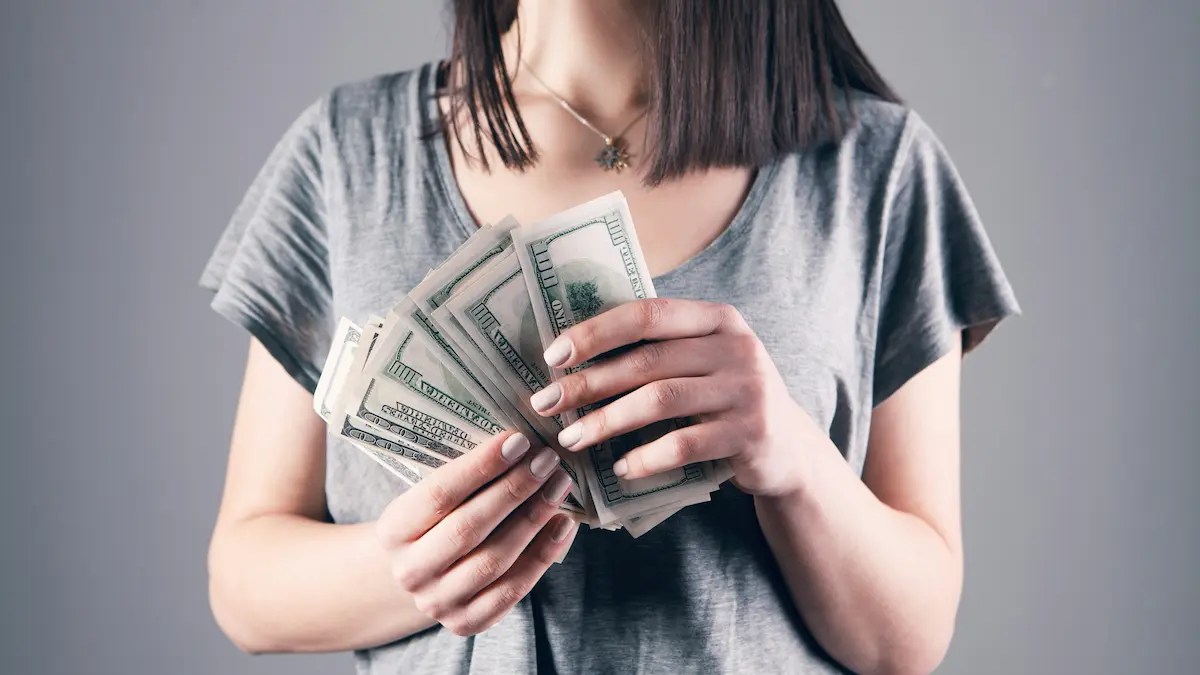 Woman holding cash symbolising the gender wealth gap and financial security challenges faced by women at work.