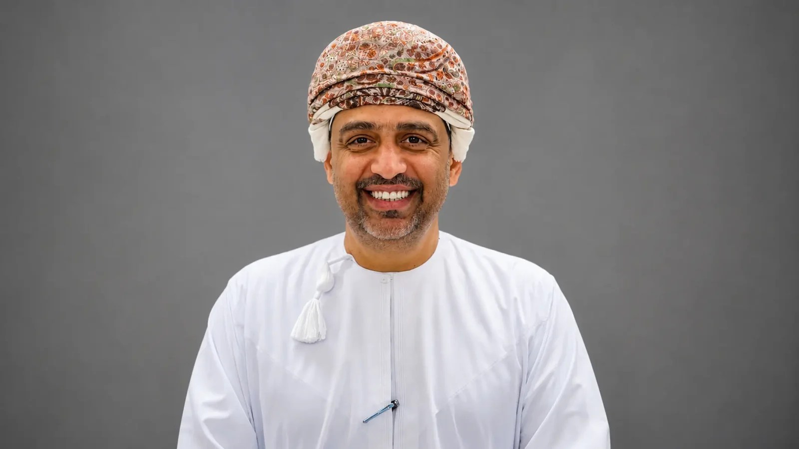 Portrait of Sulaiman Al Siyabi, Chief Executive Officer of TRANSOM Catering in Oman, wearing traditional Omani attire against a grey background.