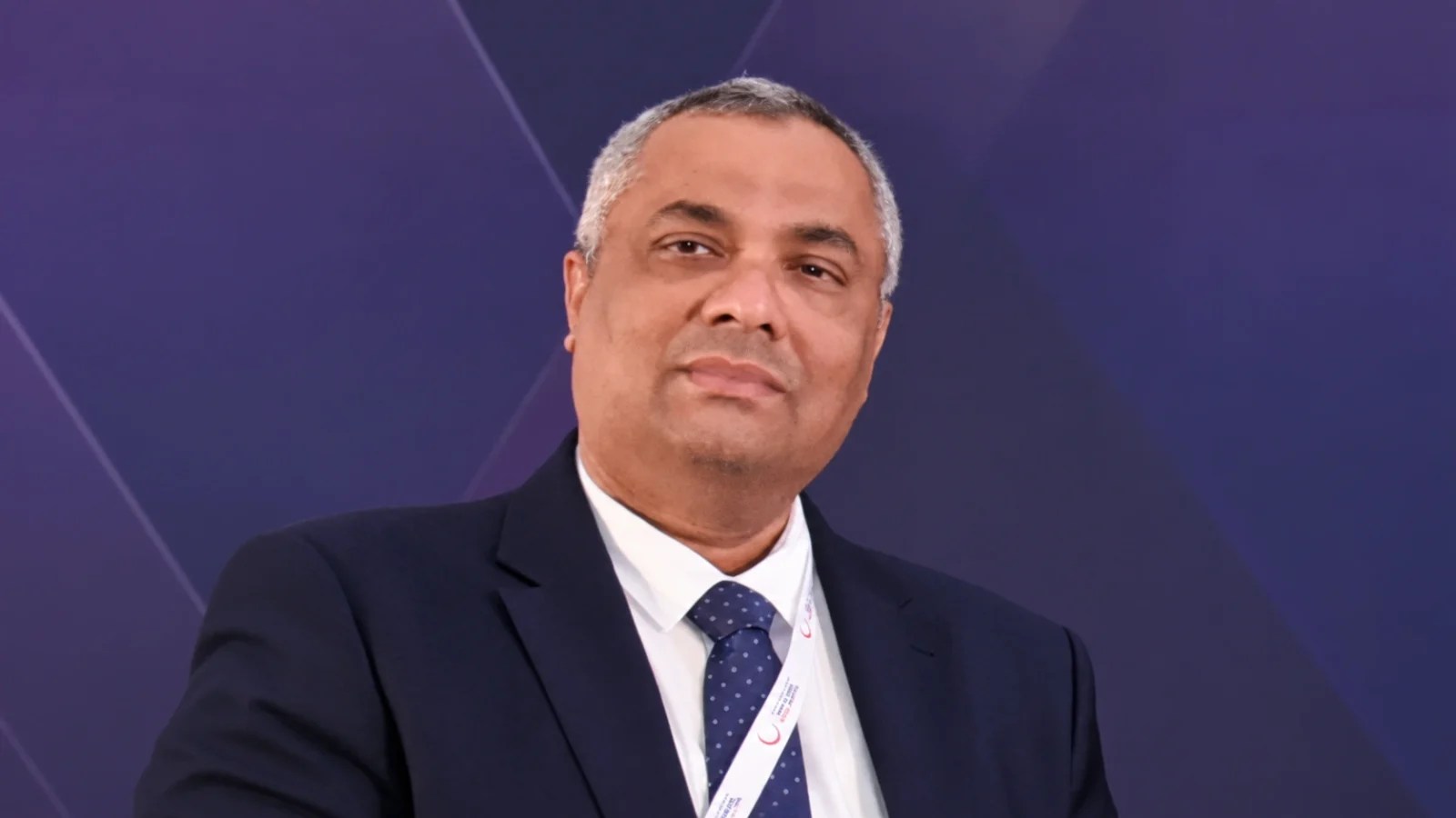 Jacob Oommen wearing a dark suit and patterned tie at a healthcare event.