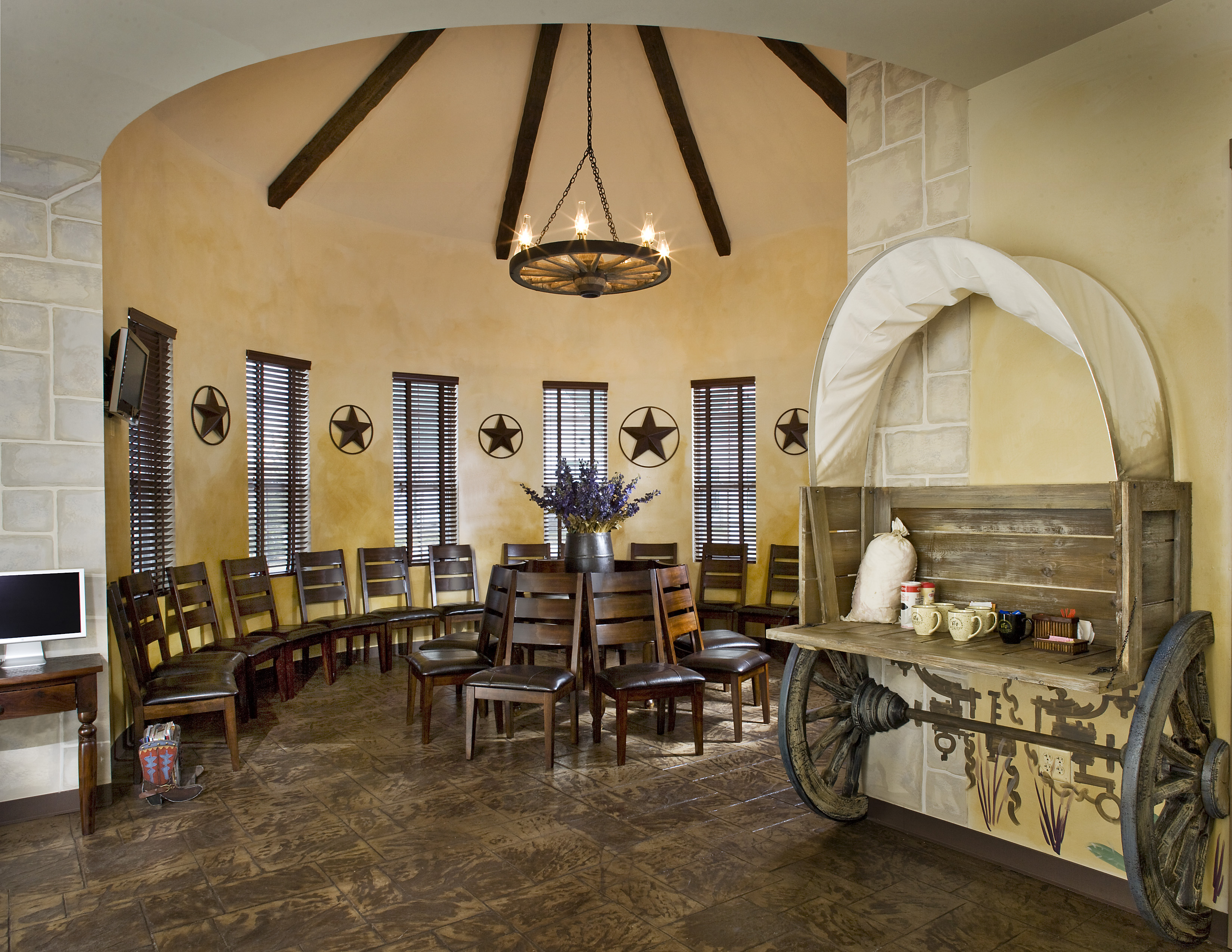 Interior view of a circular meeting room with wooden chairs arranged in a semi-circle, featuring a rustic wagon display on one side and star decorations on the walls.