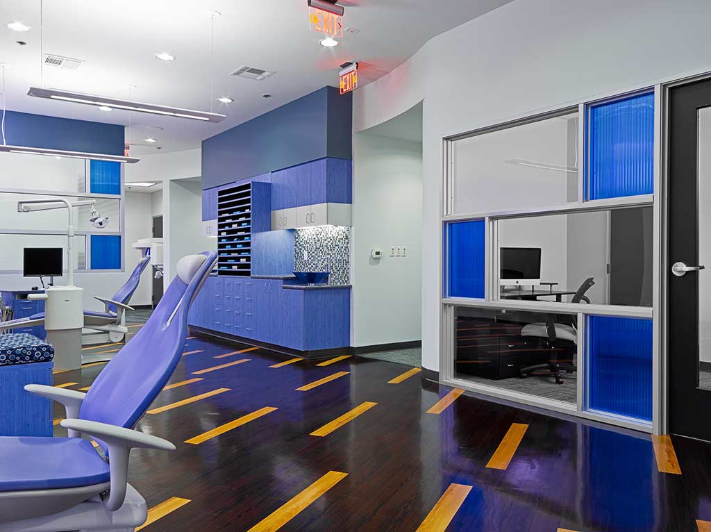 Interior view of a modern dental office featuring blue cabinetry, dental chairs, and a reception area with a computer station.