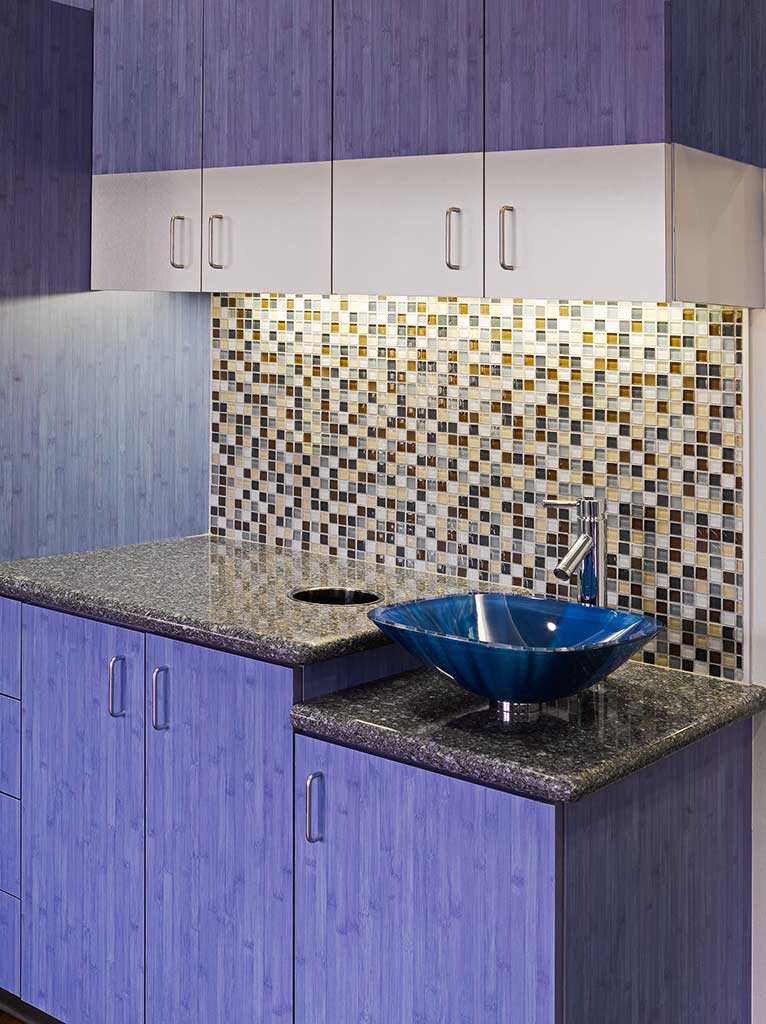 Modern kitchen design featuring blue cabinetry, a stylish blue vessel sink, and a mosaic backsplash with various colored tiles.