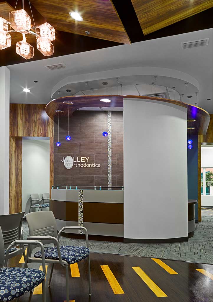 Interior view of Jolley Orthodontics office featuring modern design elements, a curved reception desk with the clinic's name, stylish lighting, and comfortable seating.