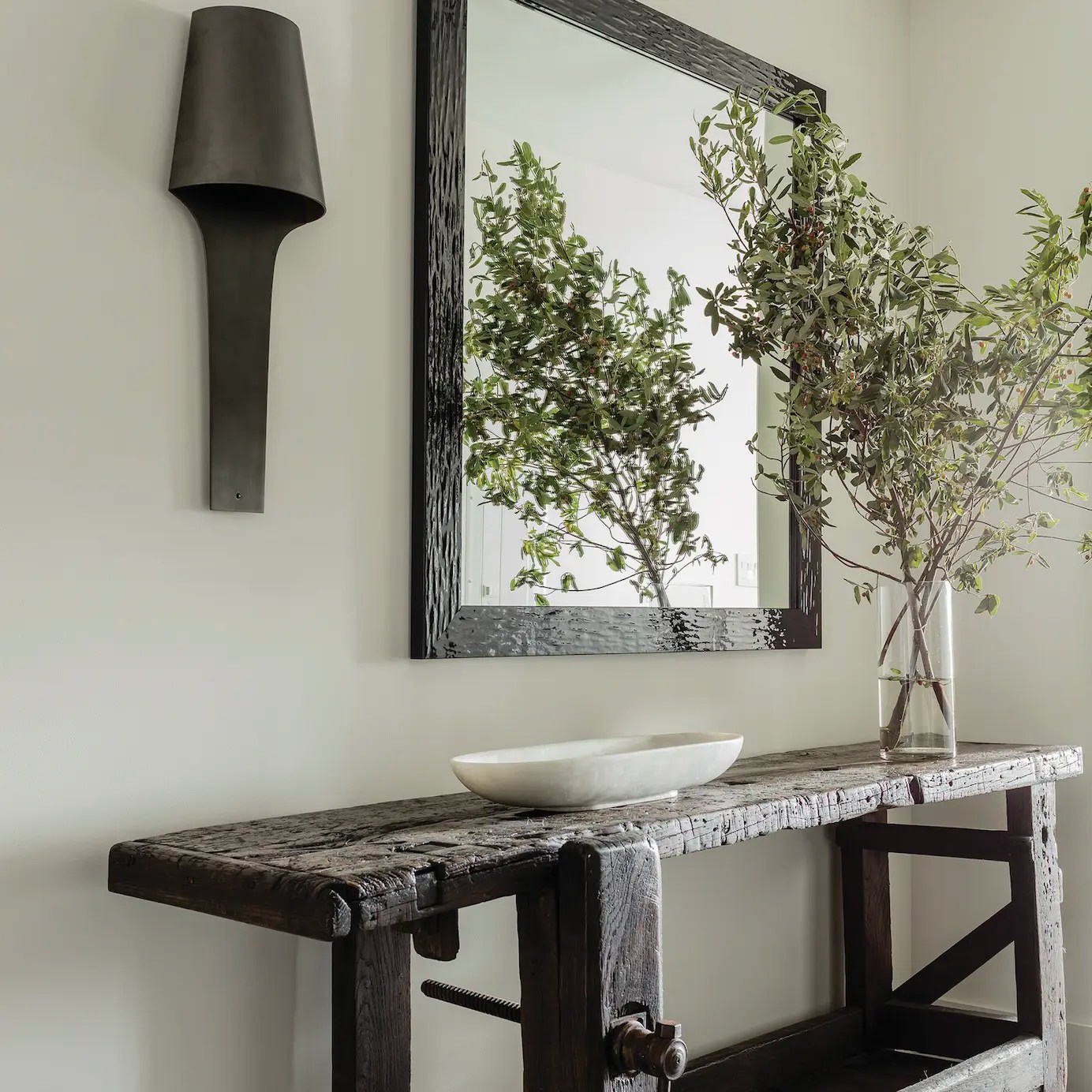 Contemporary modern foyer with bronze sconce, large mirror and vintage wood console. The console is styled with large branches and a marble bowl.