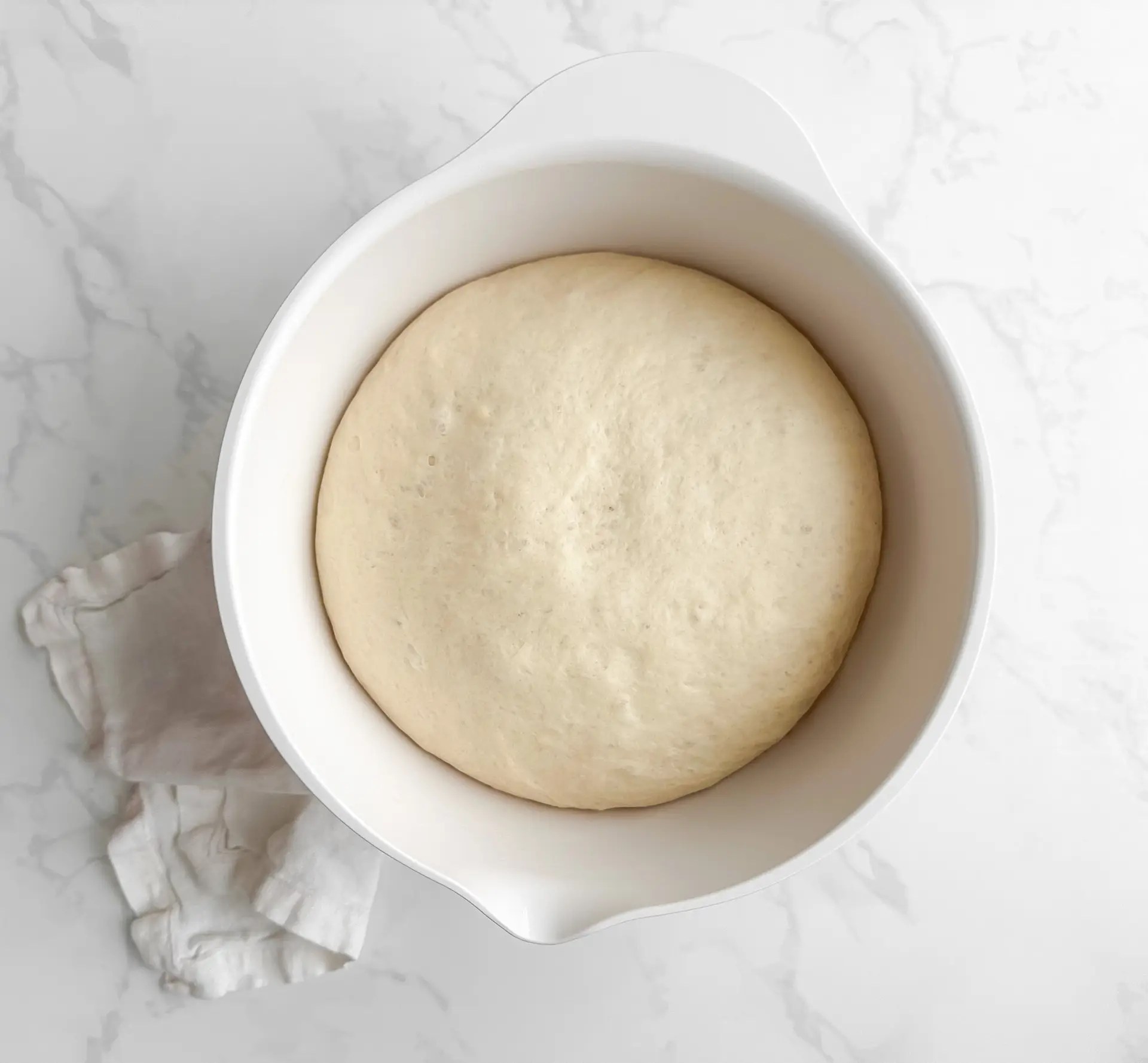 Close-up of hands pressing fingers into proofed focaccia dough to create signature dimples.