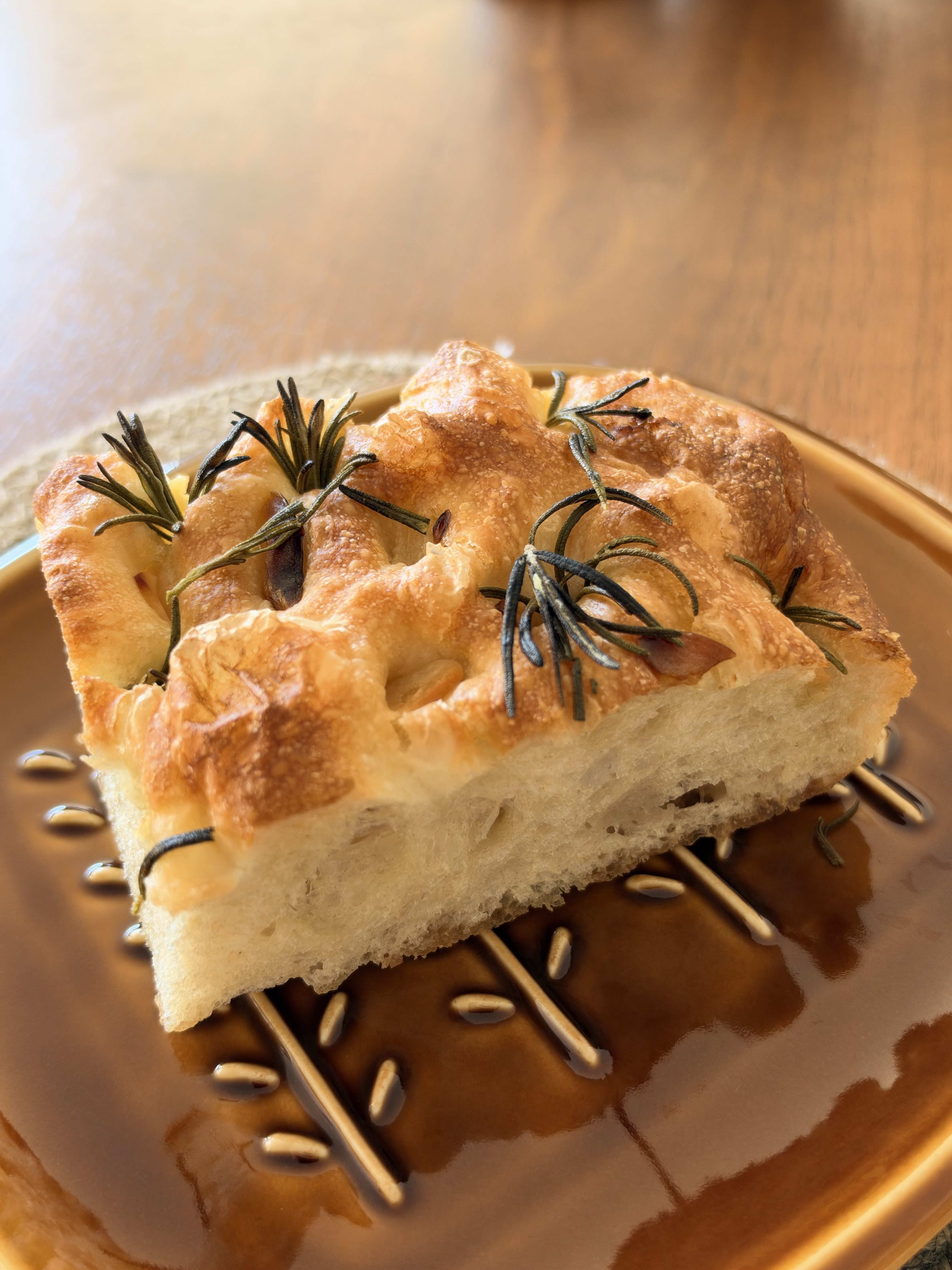 Golden garlic and rosemary focaccia with an airy crumb, served on a brown plate.