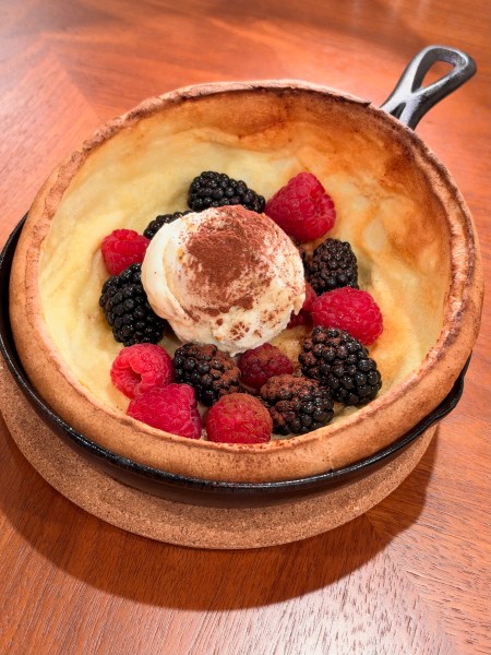 Dutch baby pancake in a cast-iron skillet topped with raspberries, blackberries and a scoop of ice cream.