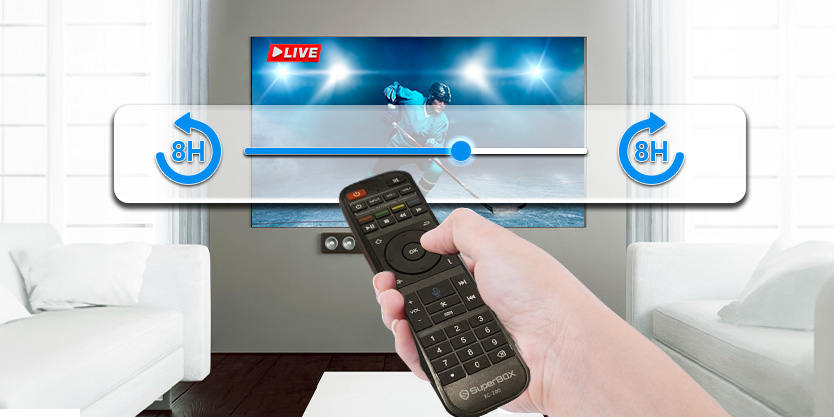 Hand holding a remote control aimed at a living room TV showing a live sports scene, with a translucent seek slider and 8H rewind/forward icons.
