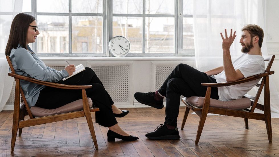 person in black pants and black shoes sitting on brown wooden chair