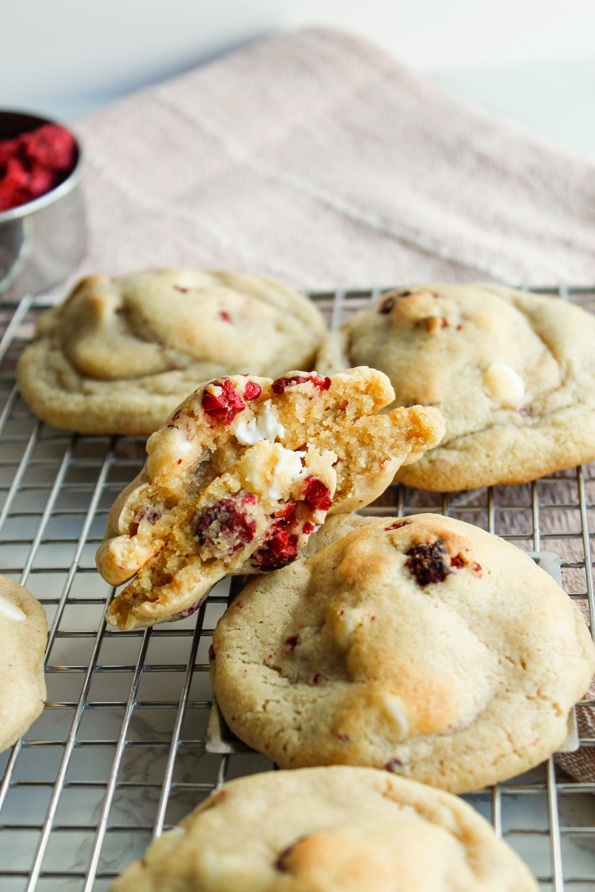 Soft white chocolate raspberry cookies with freeze-dried raspberries displayed on wire cooling rack.
