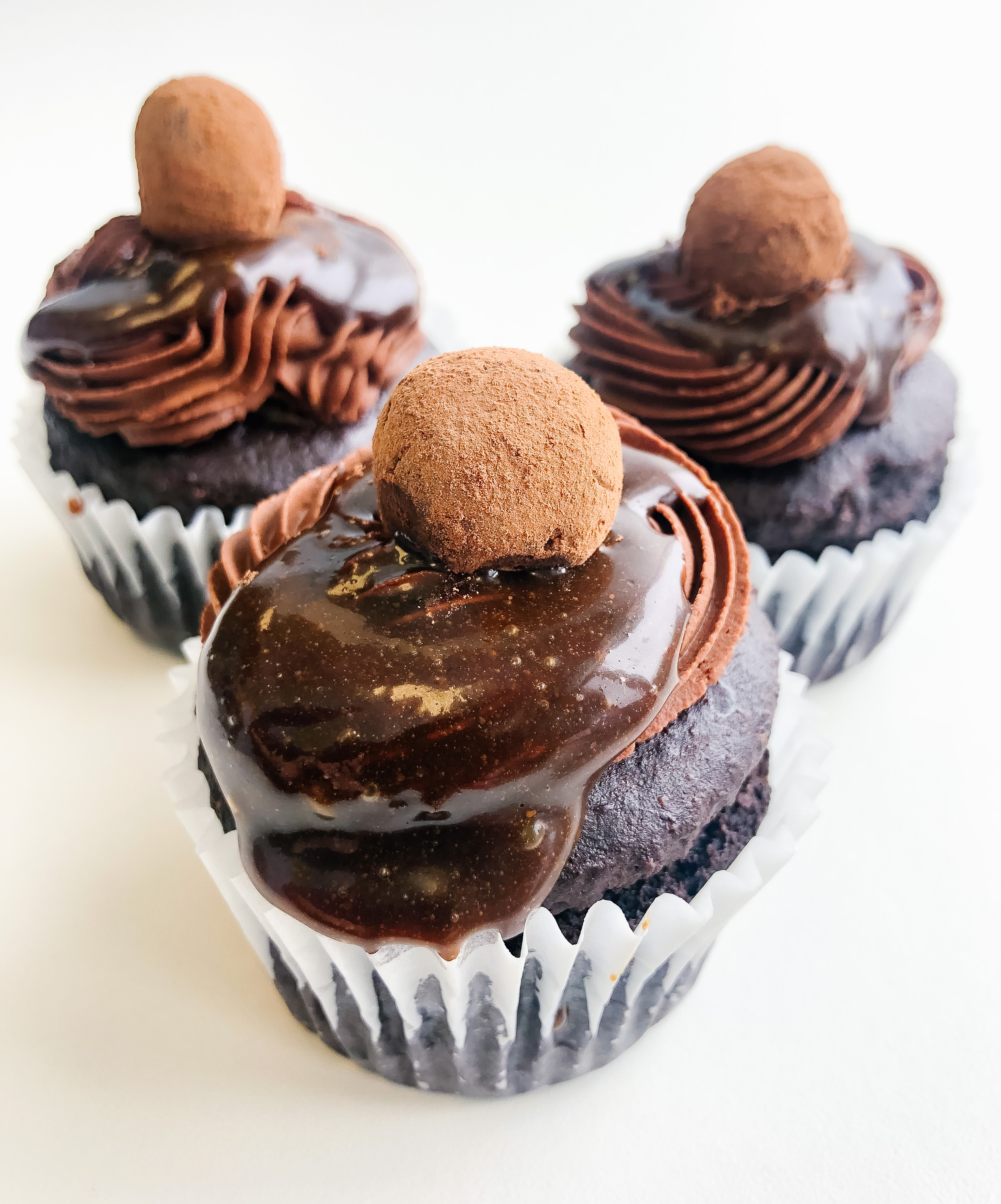 Front angle view of chocolate cupcake trio with chocolate frosting, caramel sauce, topped with chocolate truffle