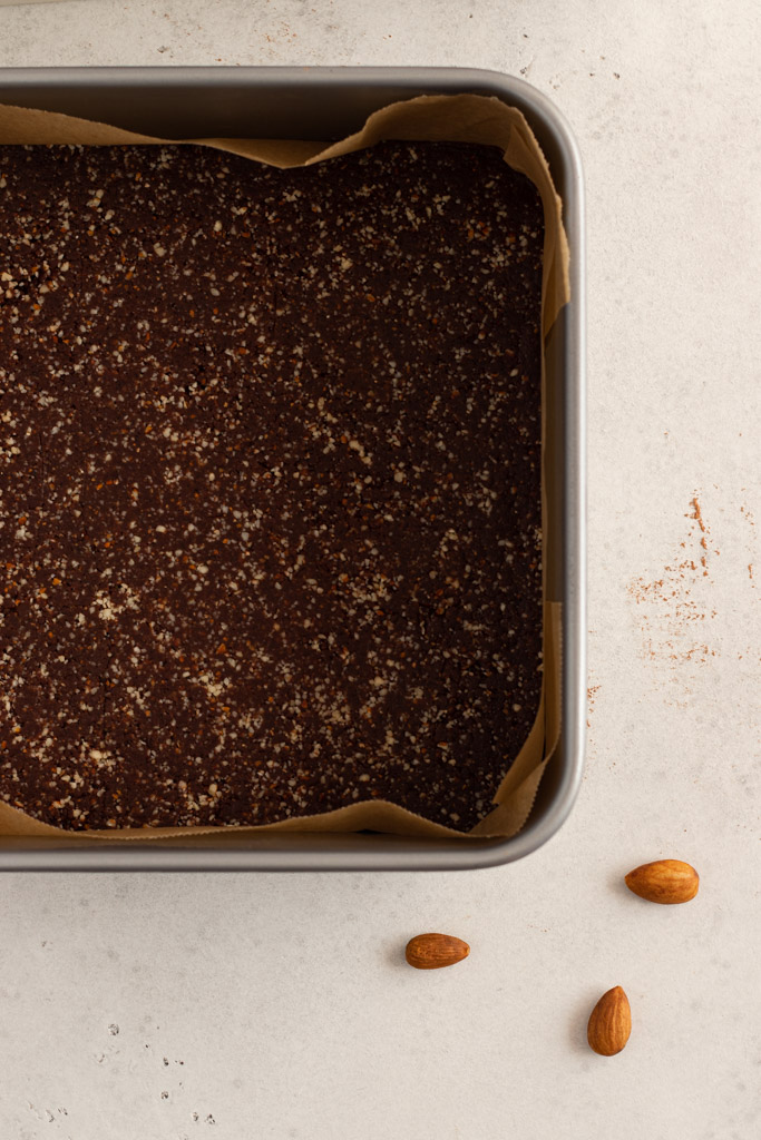 A lined square tin with the almond, date and cacao base pressed in.