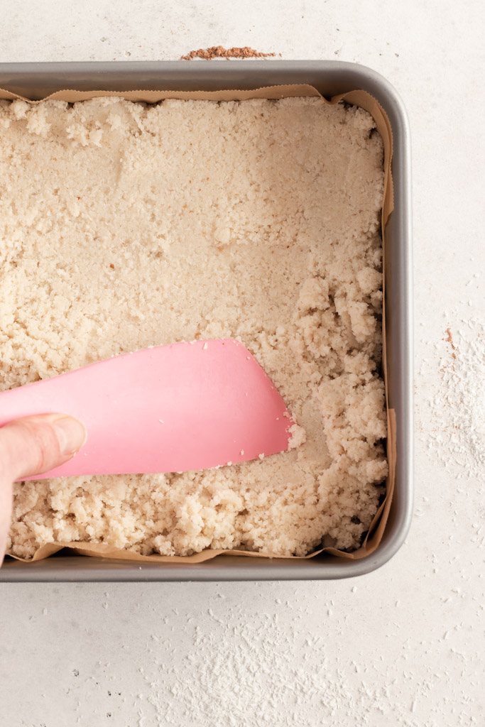 The coconut centre being pressed flat with a spatula, in the cake tin.