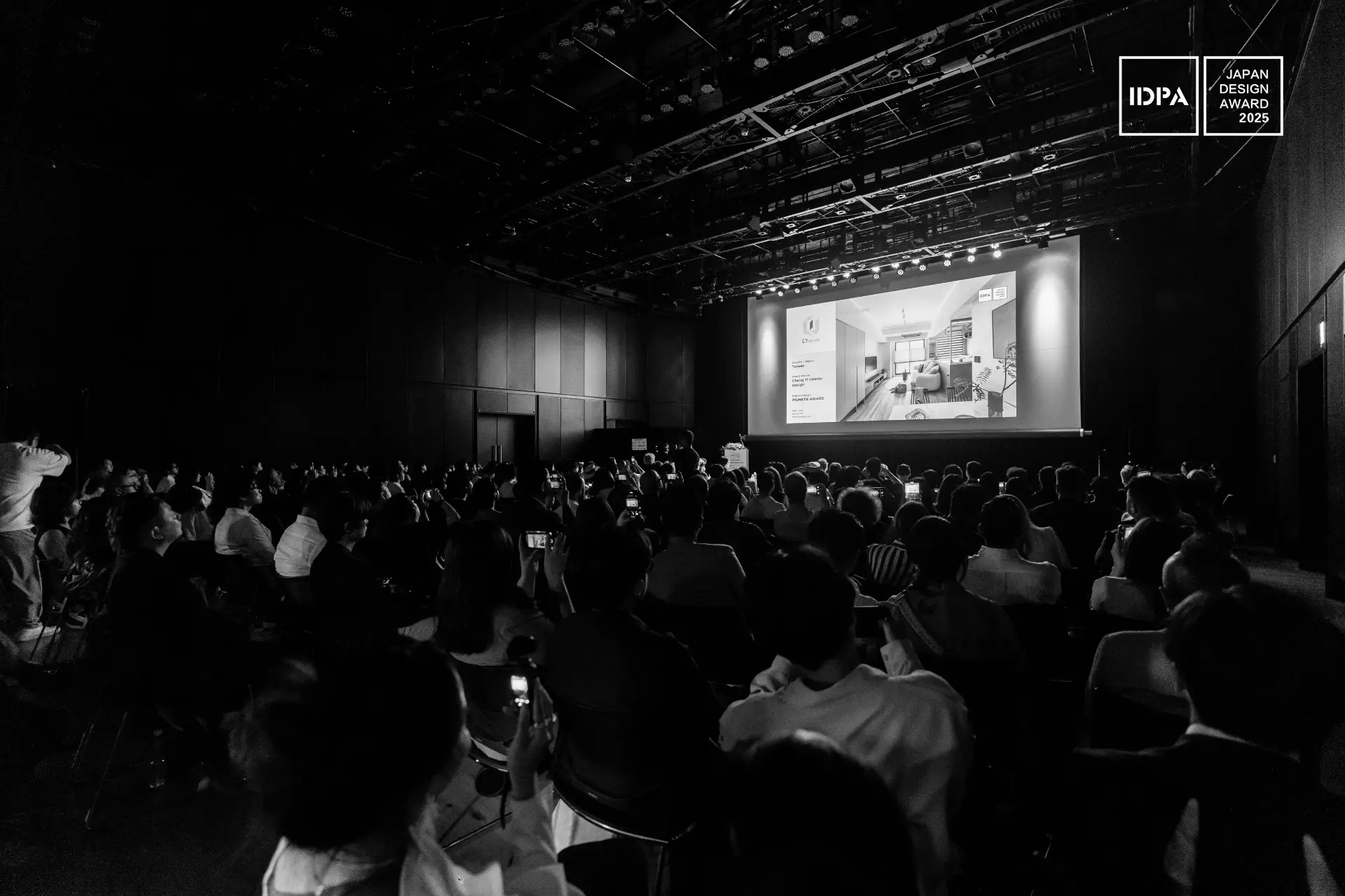 Un numeroso público sentado en un auditorio oscuro observa una presentación proyectada en una pantalla; en una esquina se ve el logotipo del Japan Design Award 2023.
