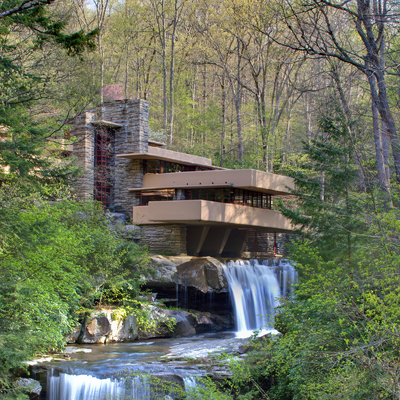 Exterior view of Frank Lloyd Wright's Fallingwater in Mill Run, Pennsylvania, during spring, showcasing its famous cantilevered concrete terraces over a waterfall surrounded by lush green foliage.