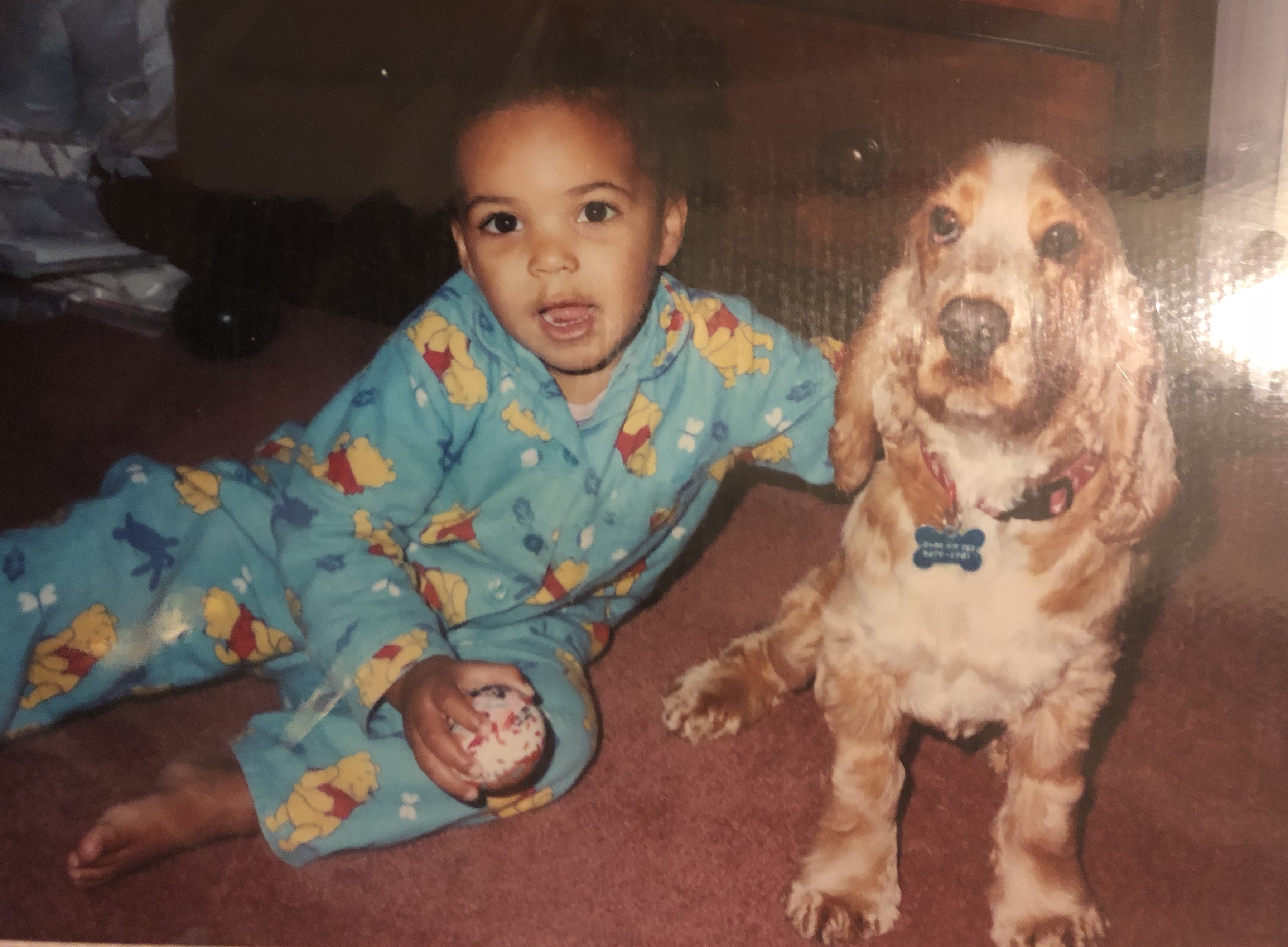 Ally Malcolm as a little girl, wearing pyjamas and sitting on the floor with a spaniel dog