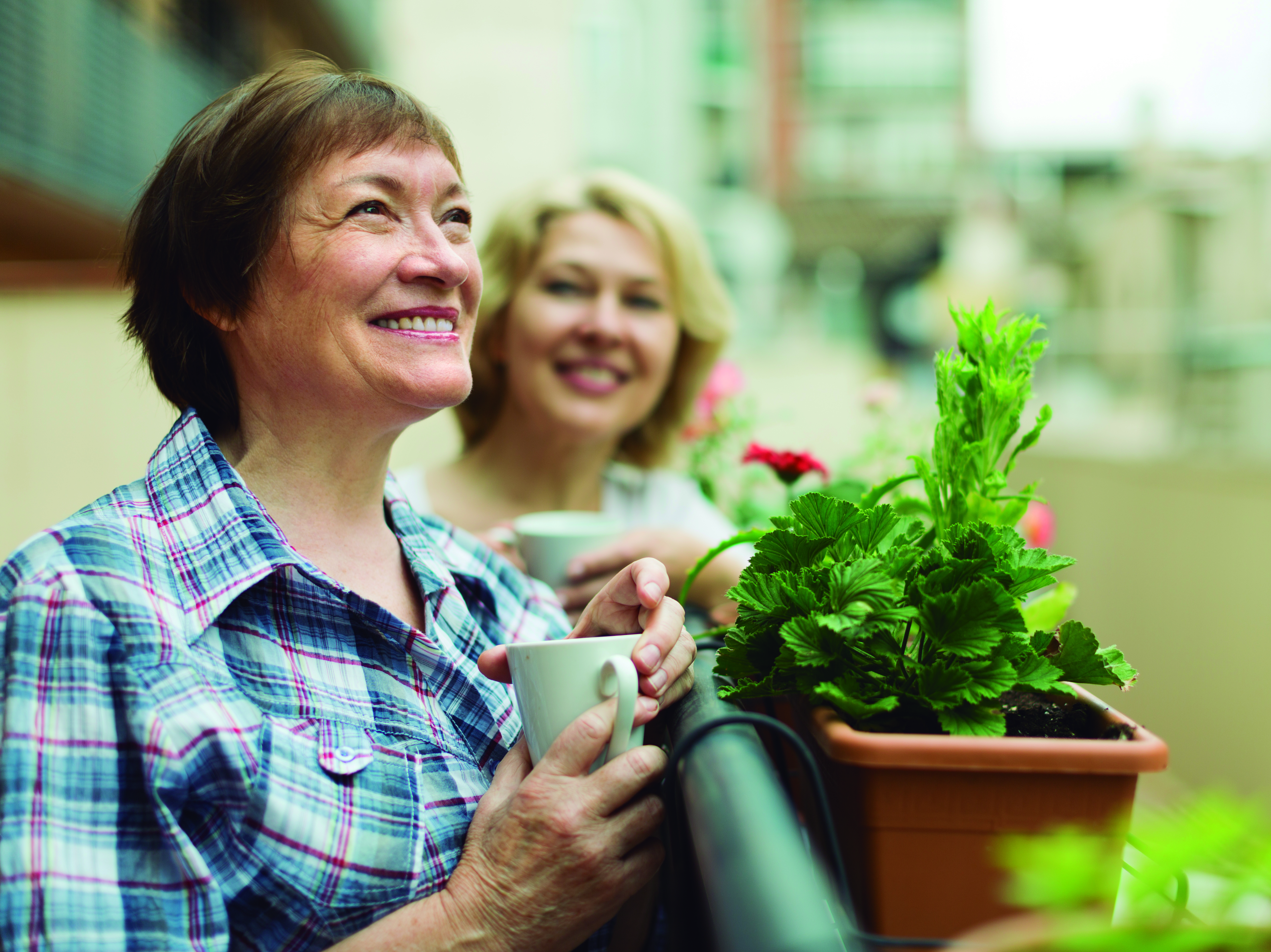 Smiling senior women staying on balcony with cup of coffee in hands