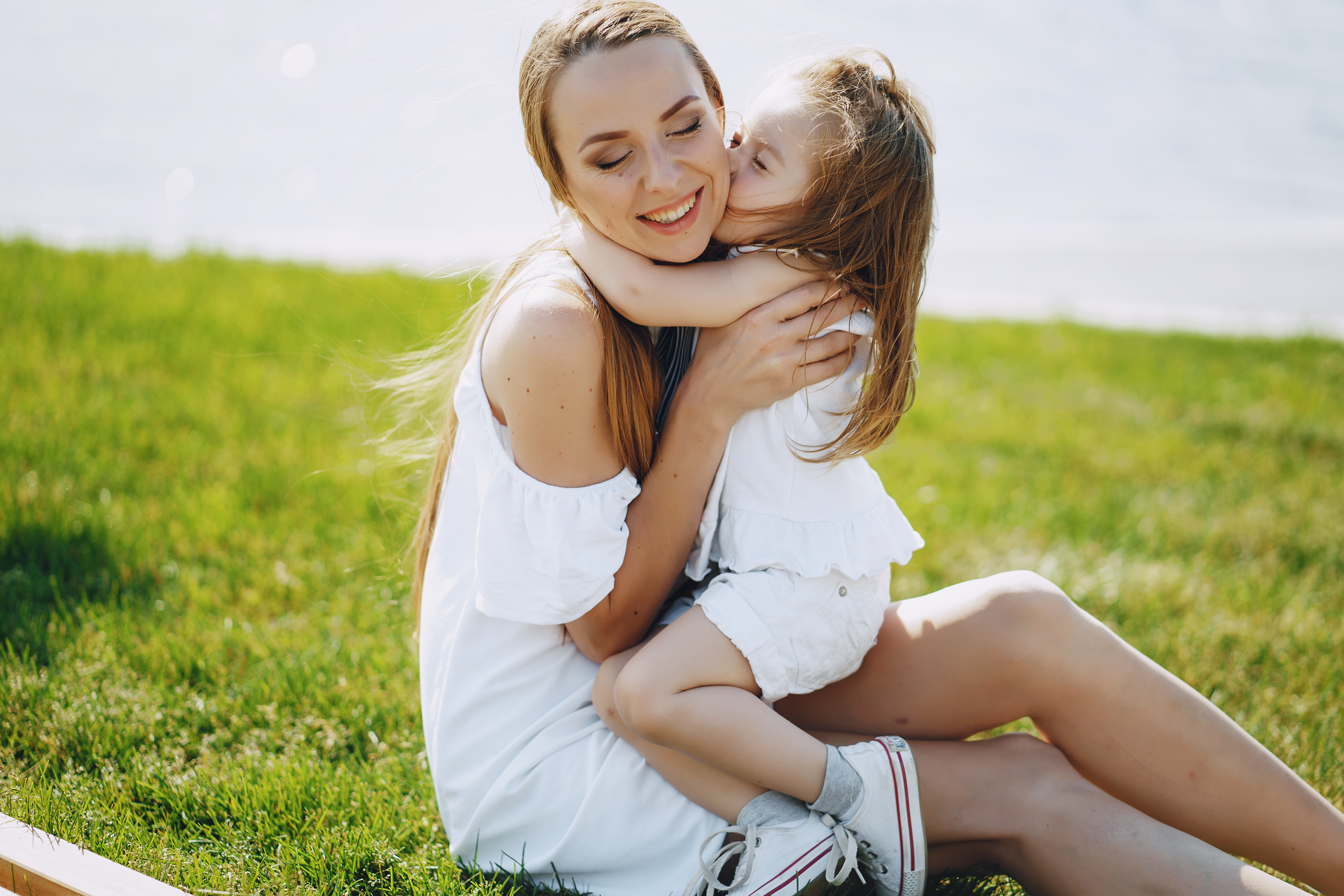 a beautiful young long-haired mom sitting in the park with her beautiful little daughter