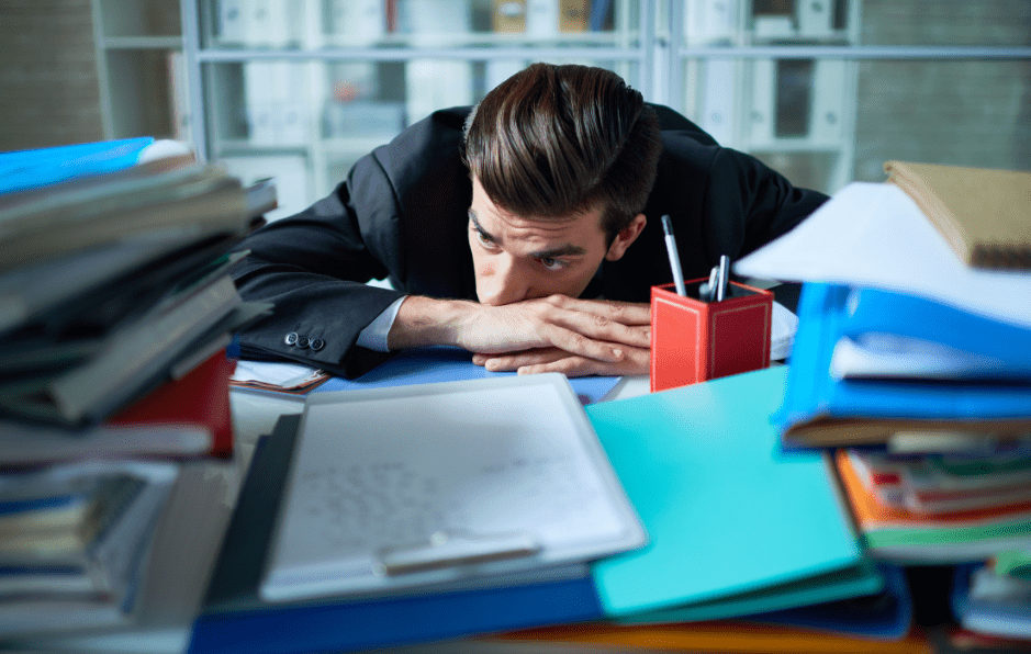 Man leaning on desk looking overwhelmed as he has too much work to do.