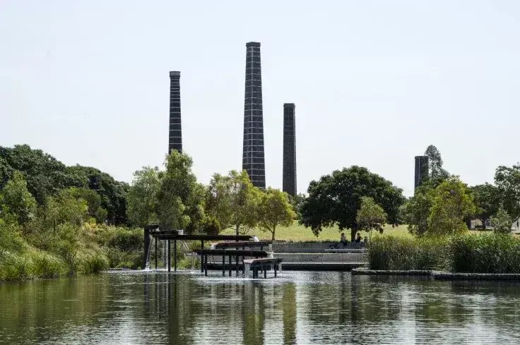 Sydney Park wetlands with reflective water, native vegetation and the historic brick kiln chimneys rising above the landscape, showcasing the park's industrial heritage and environmental transformation.